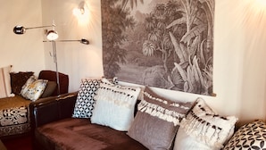 Ein gemütliches Wohnzimmer mit einem dunkelbraunen Sofa, gemusterten Kissen, einer Wandteppich und einer Stehlampe.