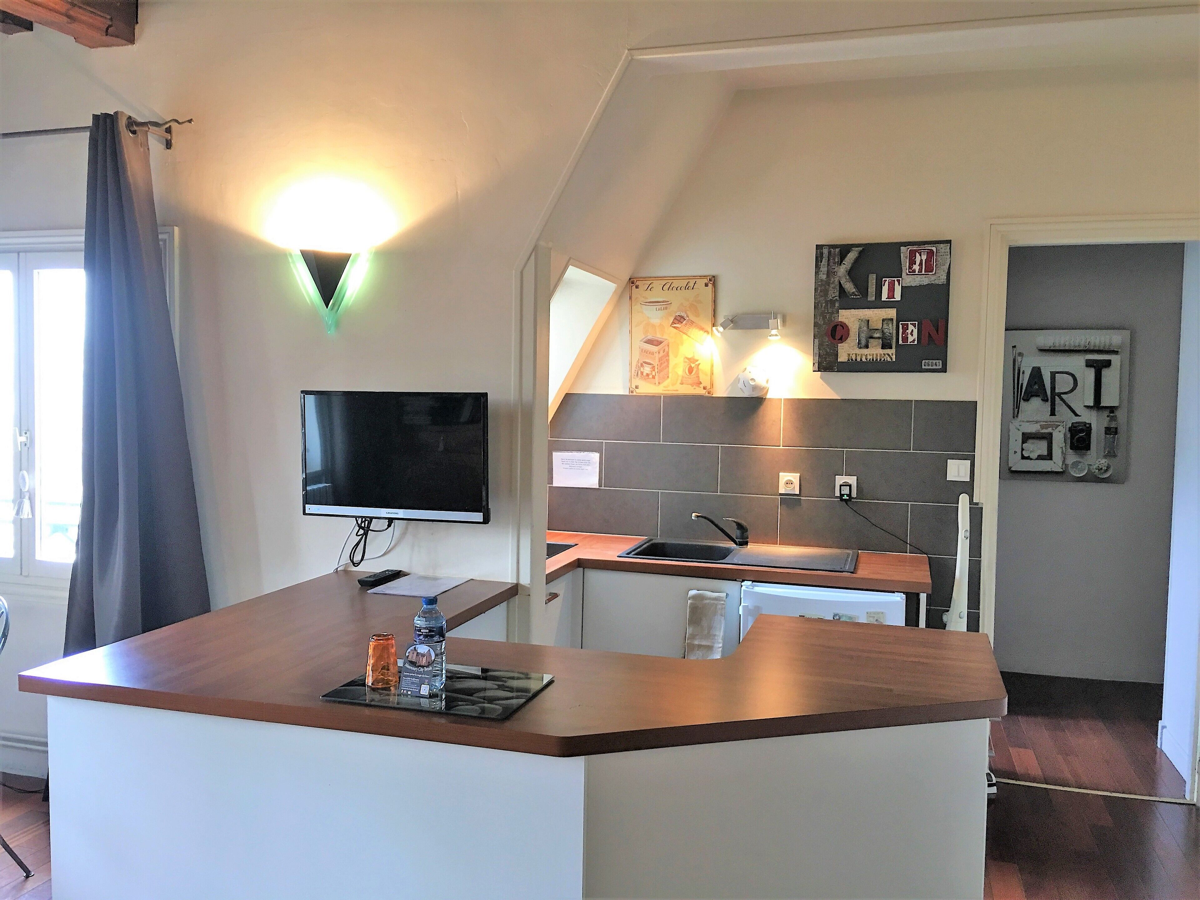 A modern kitchen with a wooden island, a flat-screen TV, and a kitchen sign.