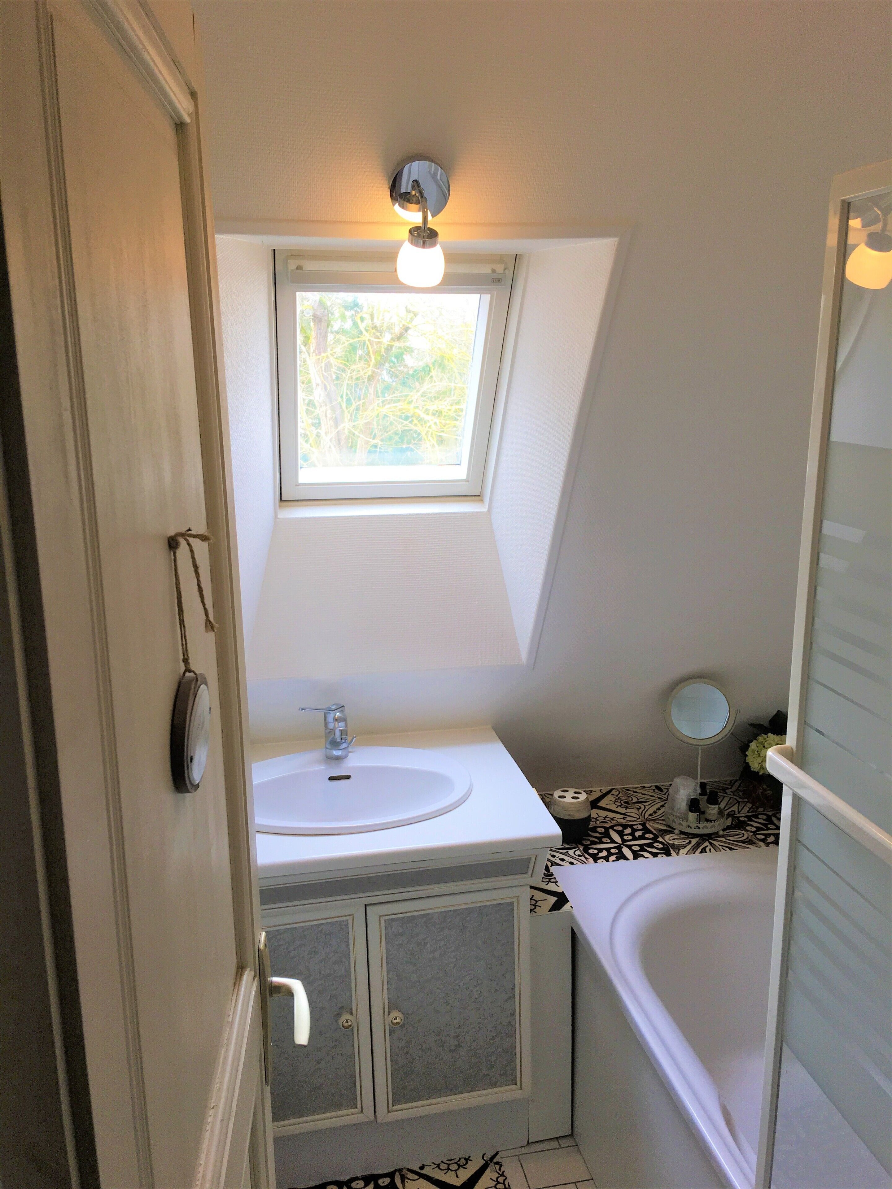 A small bathroom with a window above the sink, a bathtub, and a mirror.