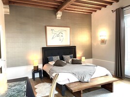 Un dormitorio con una cama grande, cabecera de madera, lámparas de noche, una obra de arte enmarcada y una ventana con cortinas.