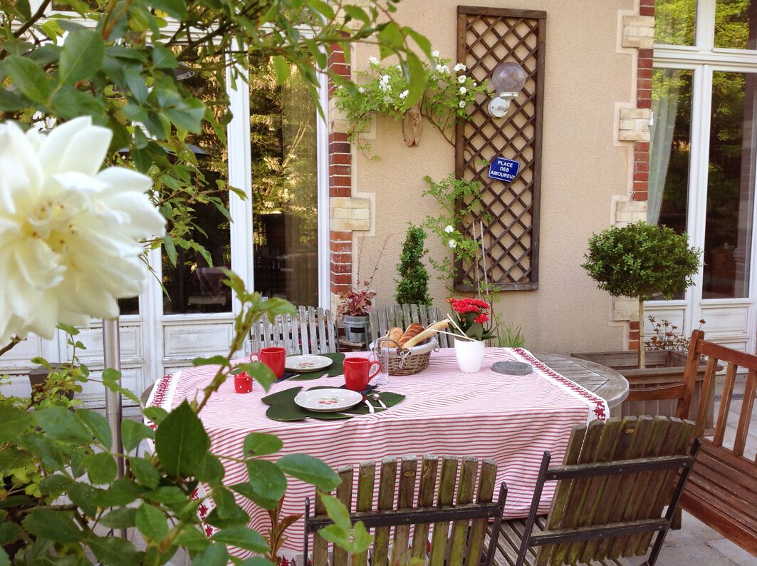 A round table with a checkered tablecloth, surrounded by wooden chairs, set outdoors with a view of a building and a sign reading "PLACE DES AMOUR".