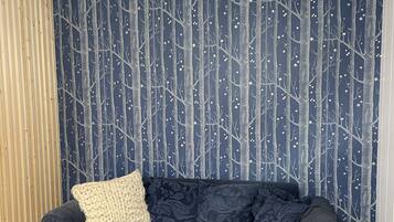 Una sala de estar con un sofá azul oscuro, un panel de pared de madera y un papel tapiz estampado.