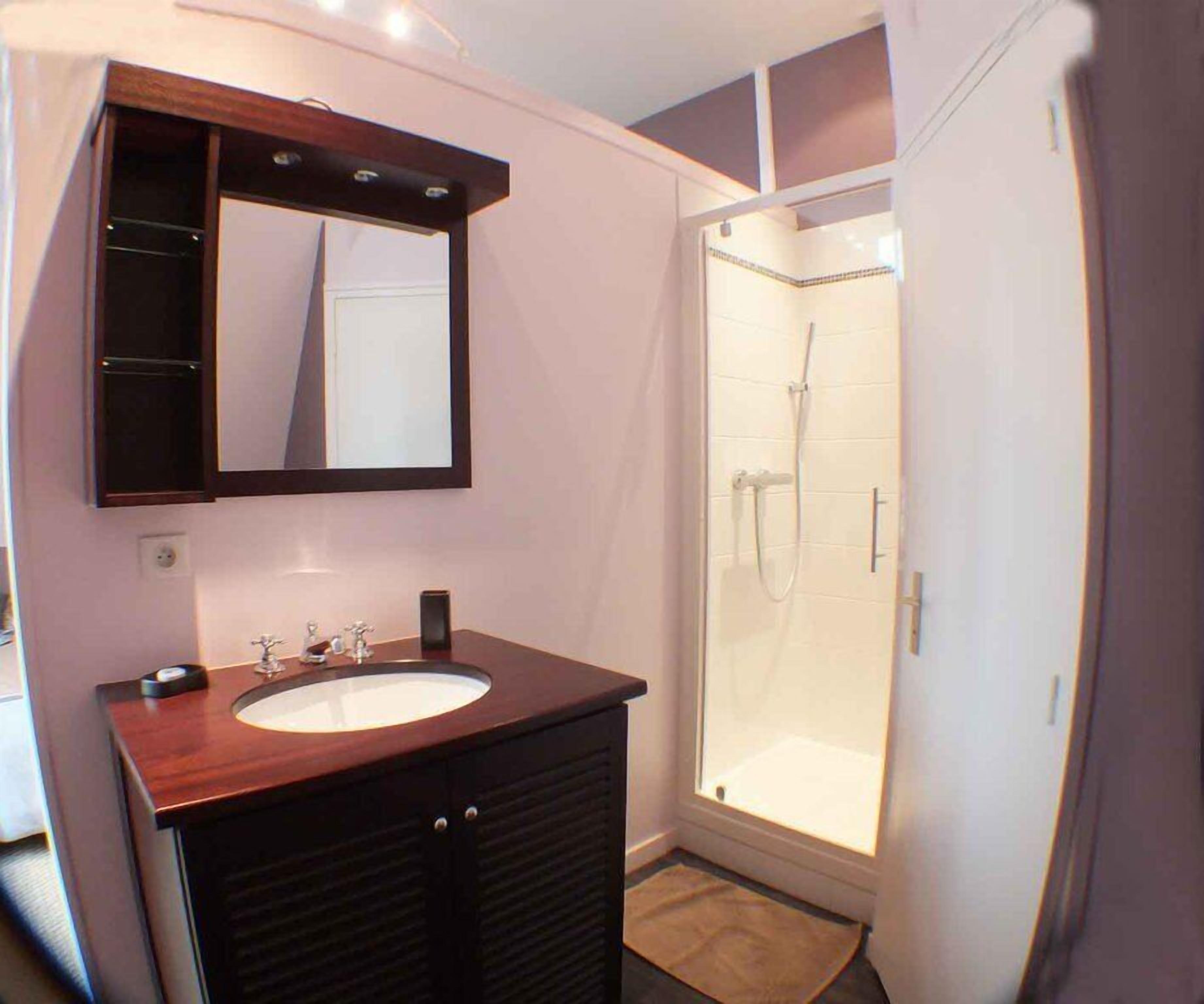 Un baño con tocador de madera, un espejo, ducha con puerta de cristal y suelo de baldosas.