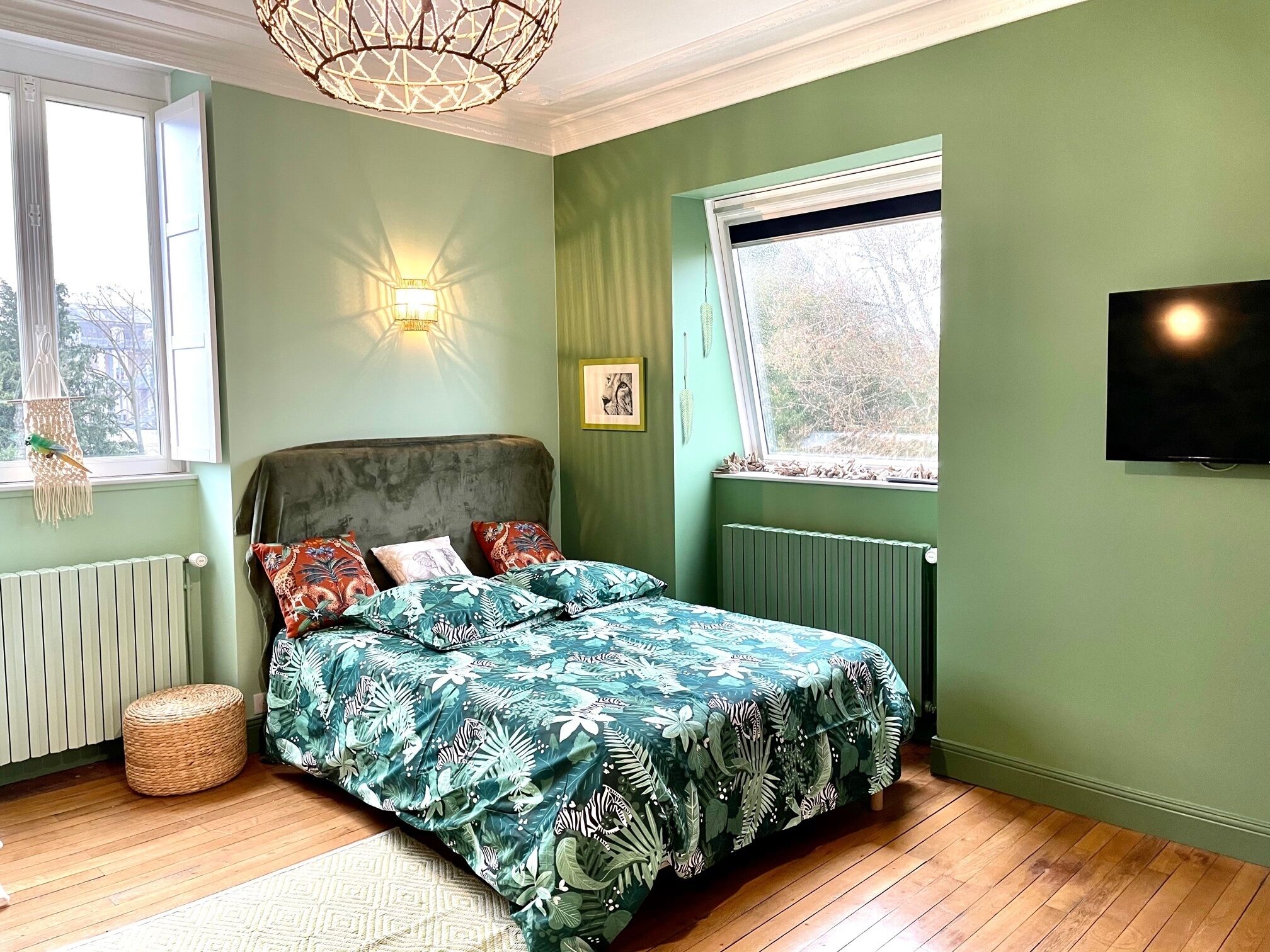 Un dormitorio con cama, un radiador, una ventana y televisor instalado en la pared.