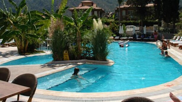 Une piscine entourée de chaises longues et de parasols, bordée de plantes tropicales et offrant une vue sur les montagnes.