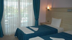 Une chambre d’hôtel avec deux lits, une table de chevet, une lampe et une fenêtre avec des rideaux.