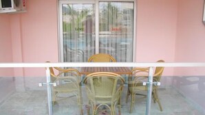 Un espace extérieur abrité par des parois de verre, avec des chaises en osier et une table en bois, où l’on peut prendre ses repas.