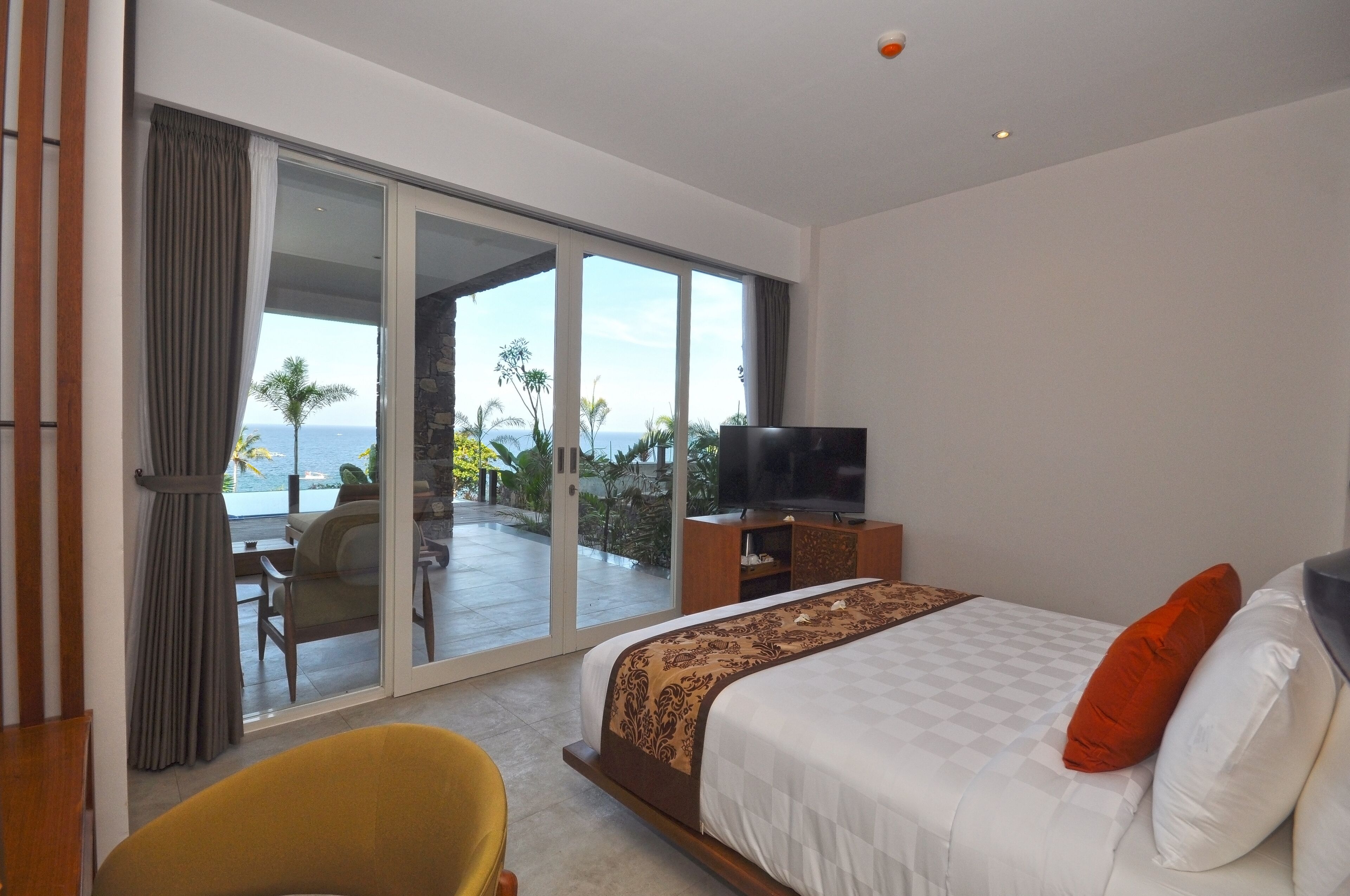 Ein Schlafzimmer mit Bett, Fernseher und Blick auf den Ozean durch eine Schiebetür.