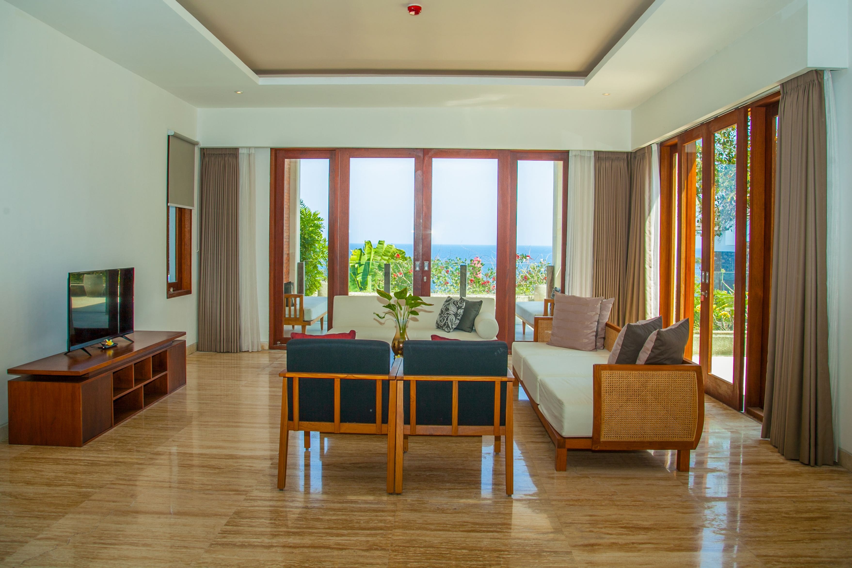 A spacious living room with a large TV, a sofa, a coffee table, and a view of the sea.