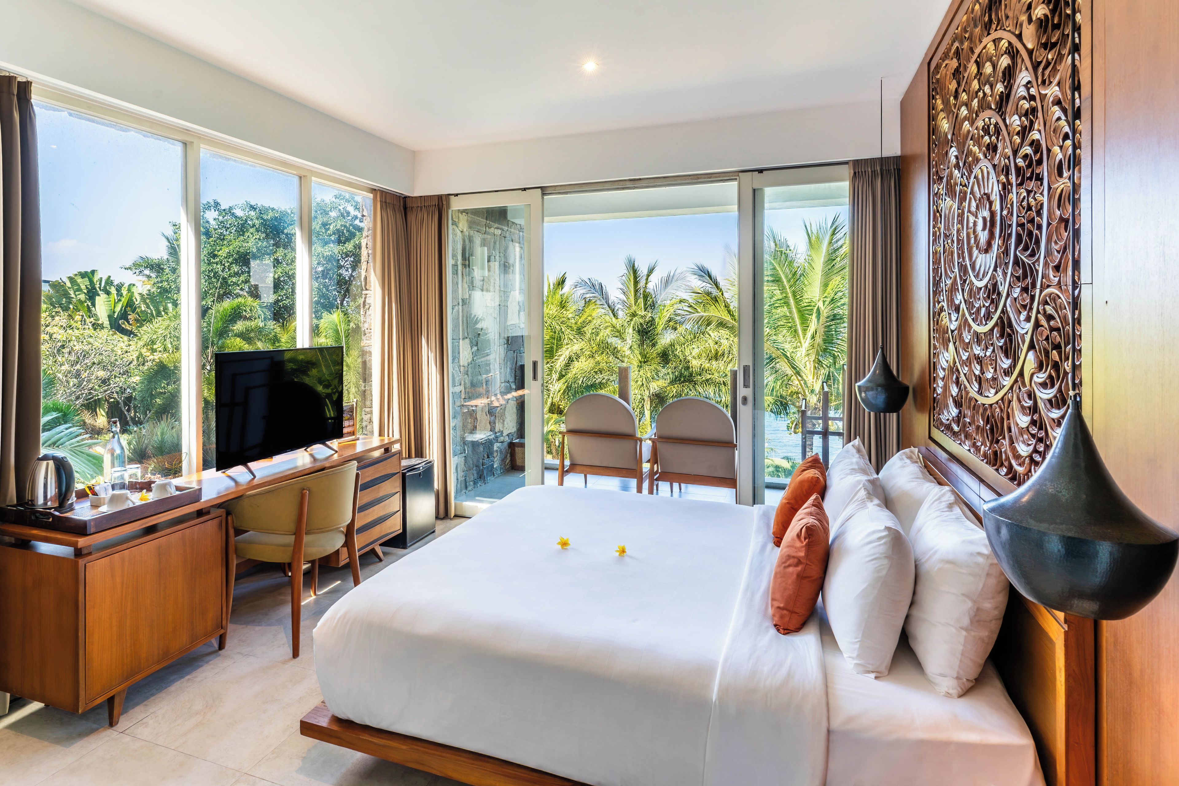 A hotel room with a large bed, a desk with a television, and a view of the outdoors.