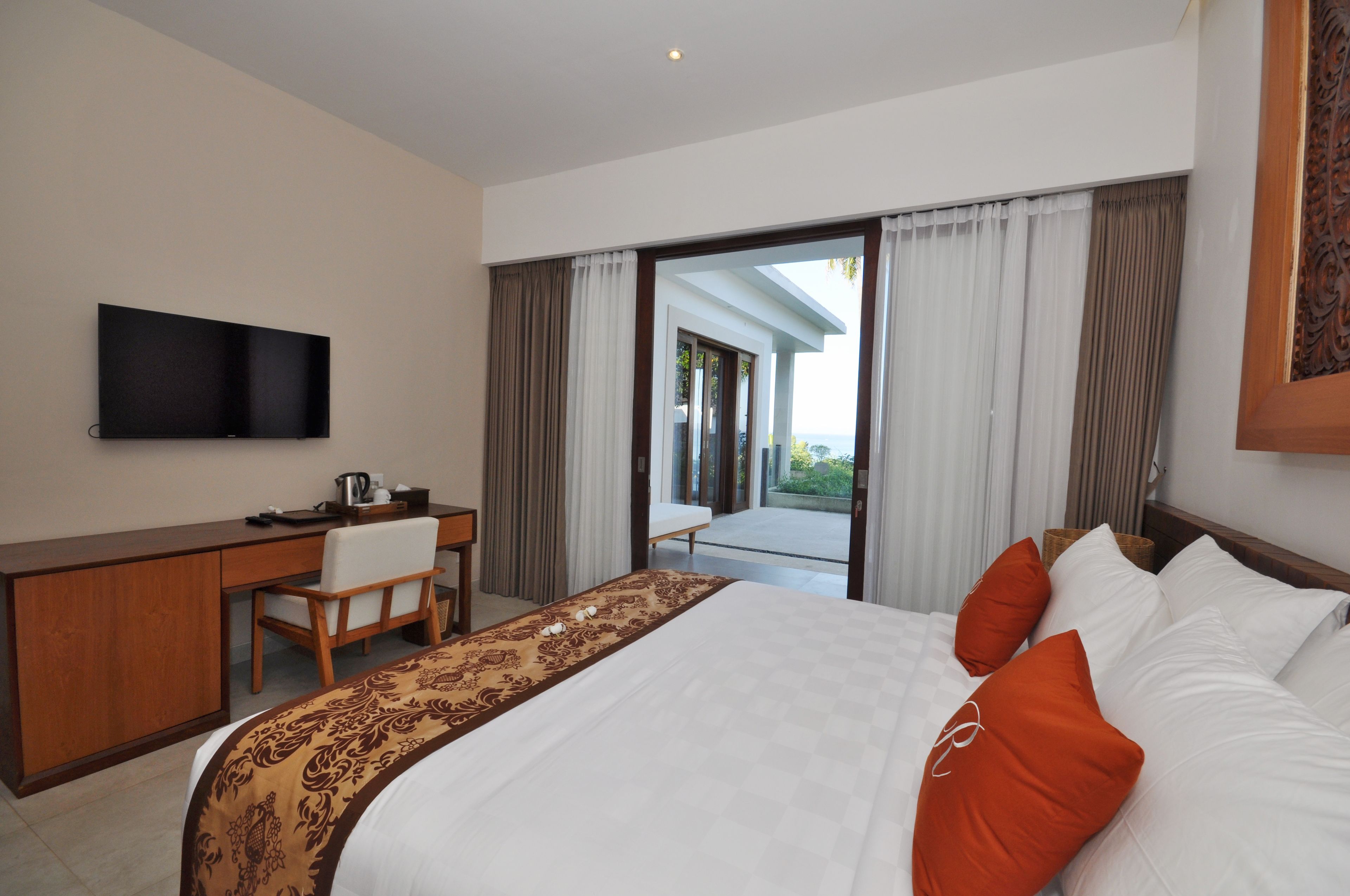 Habitación de hotel con cama, escritorio, silla, televisor y vistas al exterior.