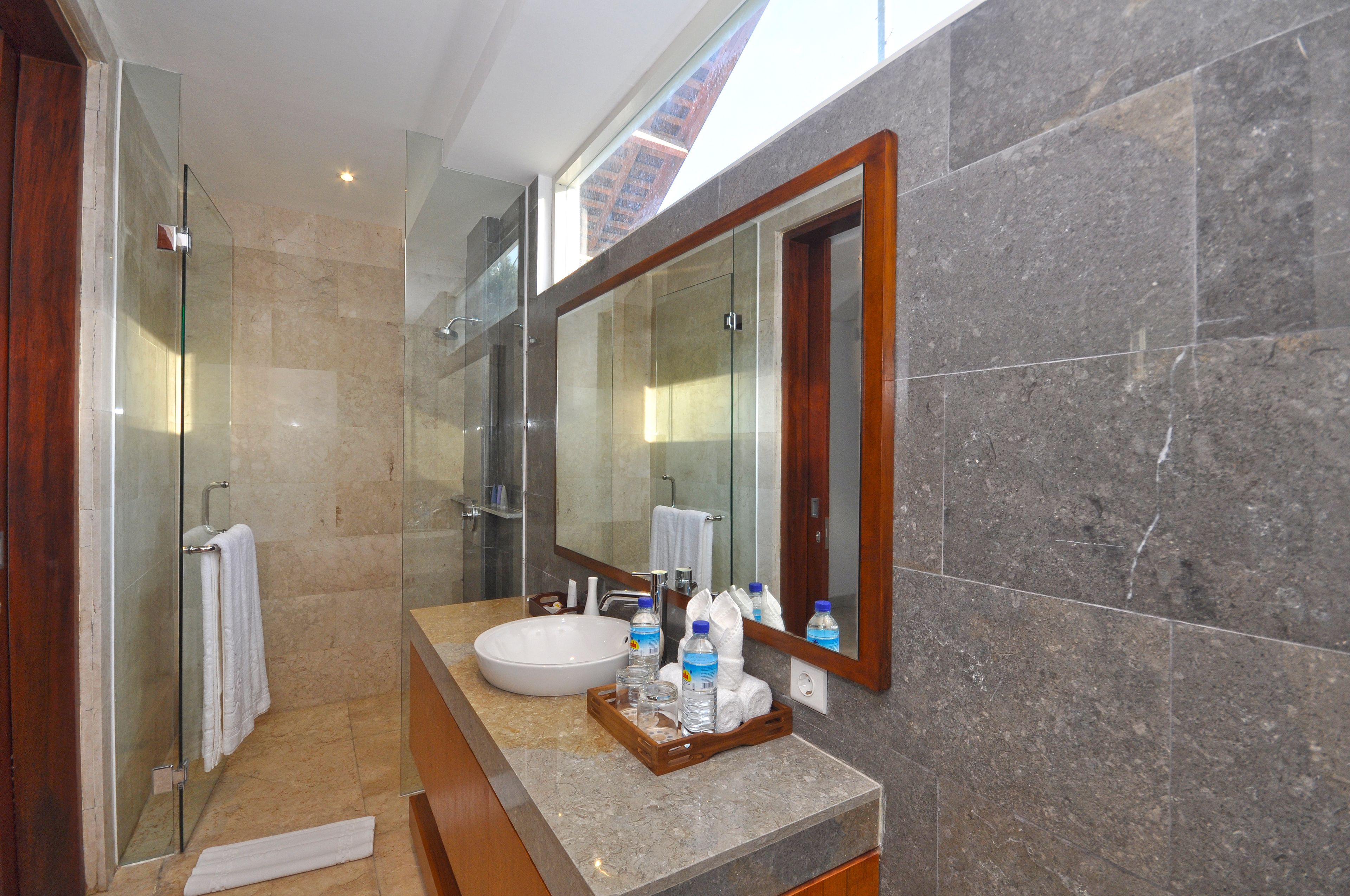 A modern bathroom with a glass shower, a large mirror, and a marble countertop.