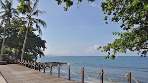 A wooden pier with rope barriers, palm trees, and a view of the ocean. - Rajavilla Lombok Resort (Senggigi)