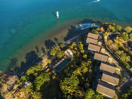 Vue aérienne d’une propriété située sur la côte, avec une piscine, plusieurs bâtiments et un phare visible au loin.