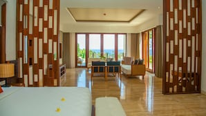 A hotel room with a large bed, a seating area with a view, and a wooden partition. - Rajavilla Lombok Resort (Senggigi)