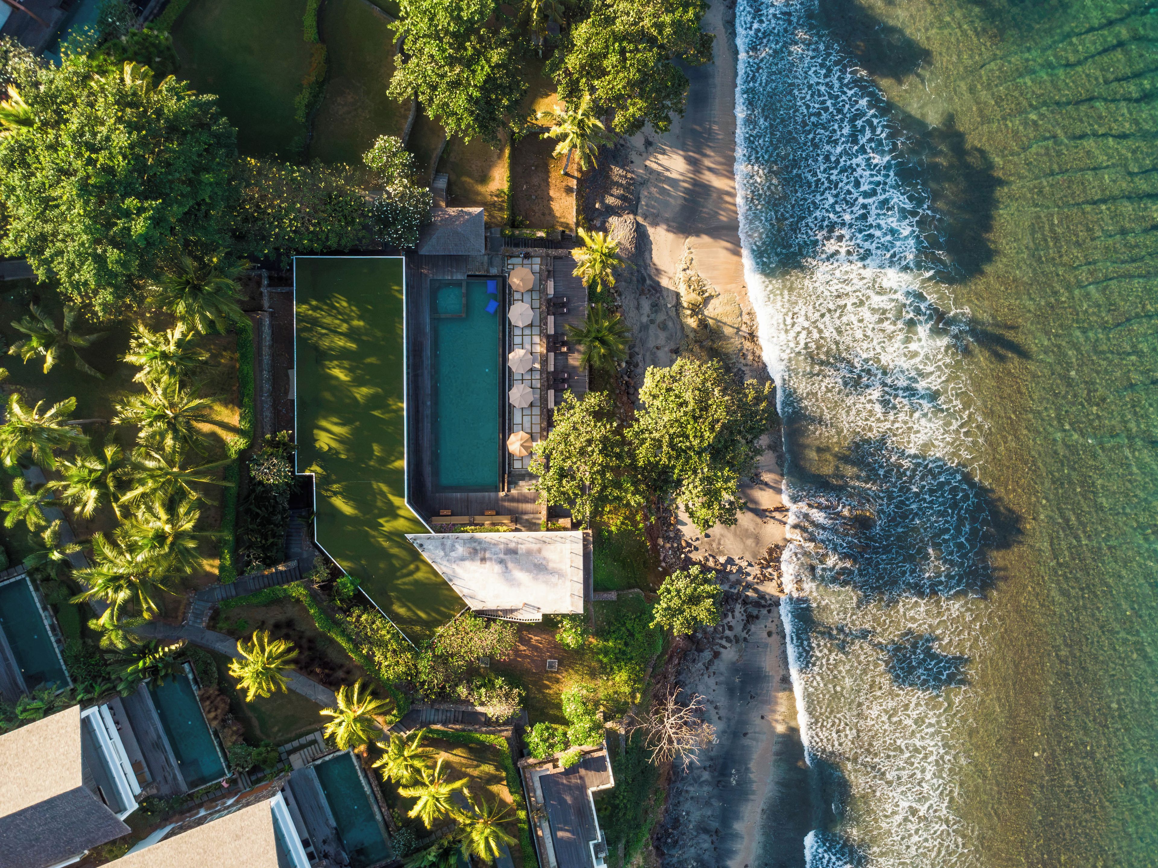 Vista aérea de un resort con piscina, zona de descanso y acceso a la playa.