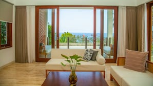A spacious living room with a large sliding glass door leading to a balcony with a view of the sea. - Rajavilla Lombok Resort (Senggigi)