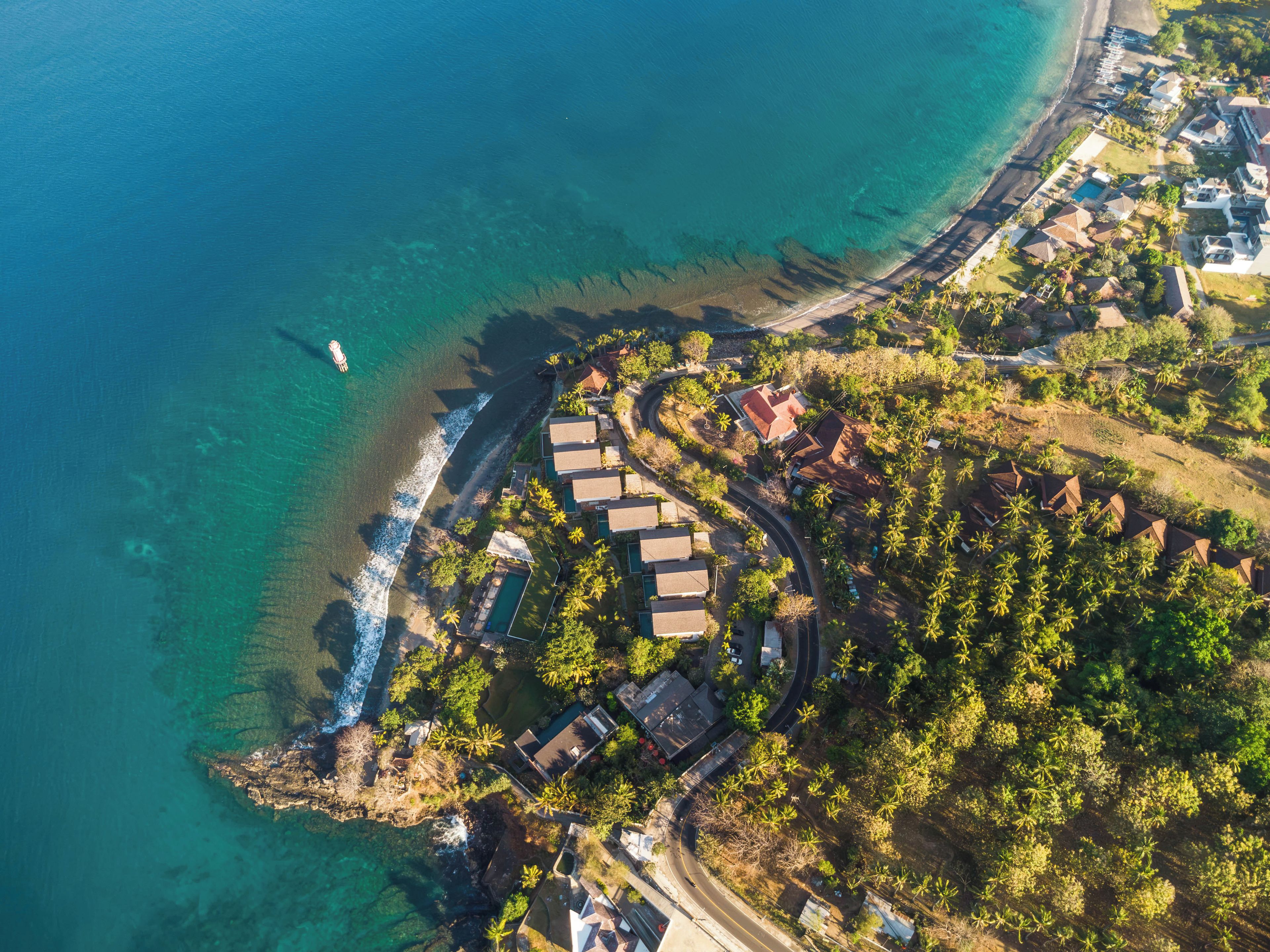 Vue aérienne d’une propriété située sur la côte, avec une route sinueuse, une piscine et une plage.