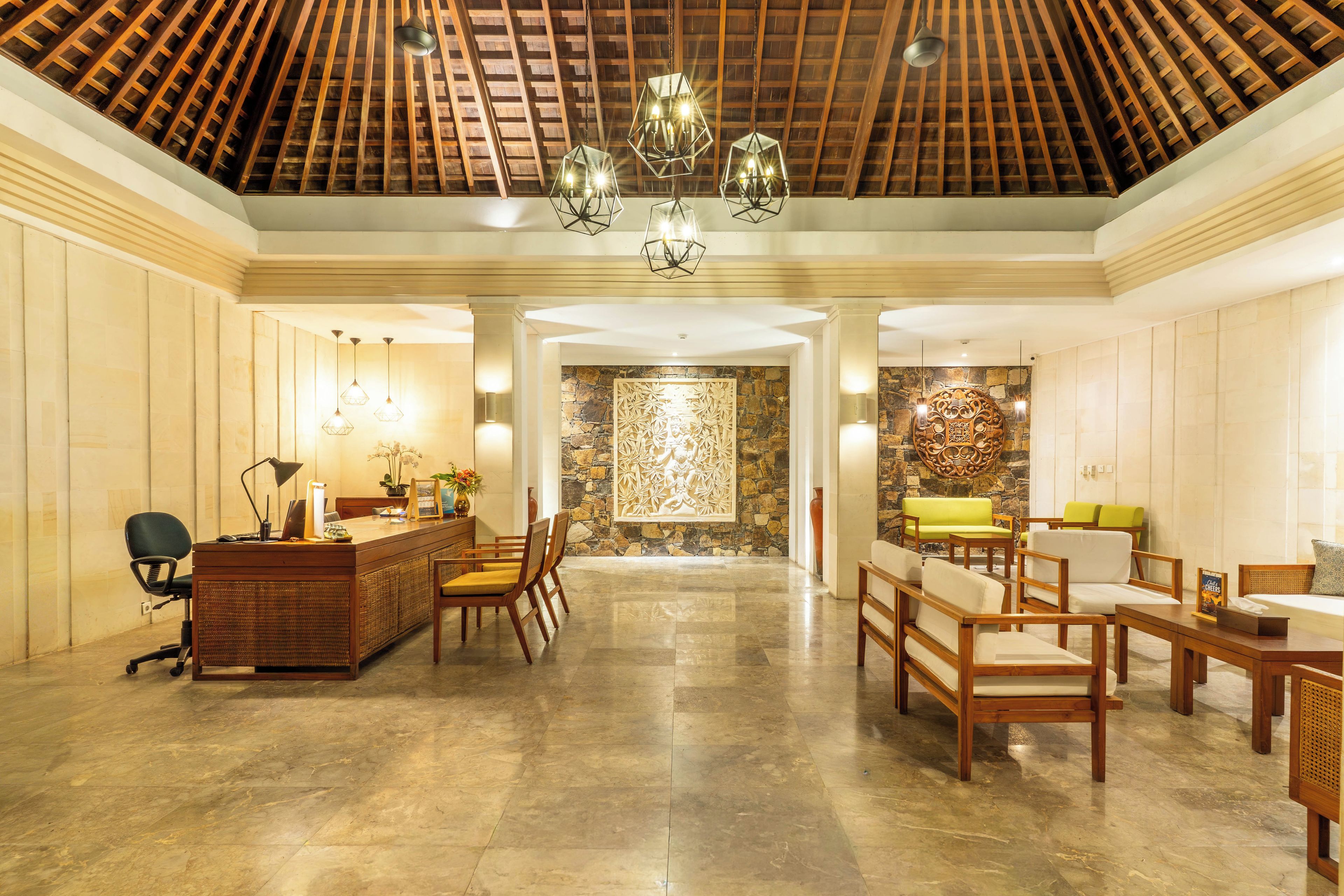 Vestíbulo de hotel con mostrador de recepción, zona de estar y pared de piedra con un panel decorativo.