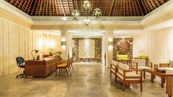 Vestíbulo de hotel con mostrador de recepción, zona de estar y pared de piedra con un panel decorativo.