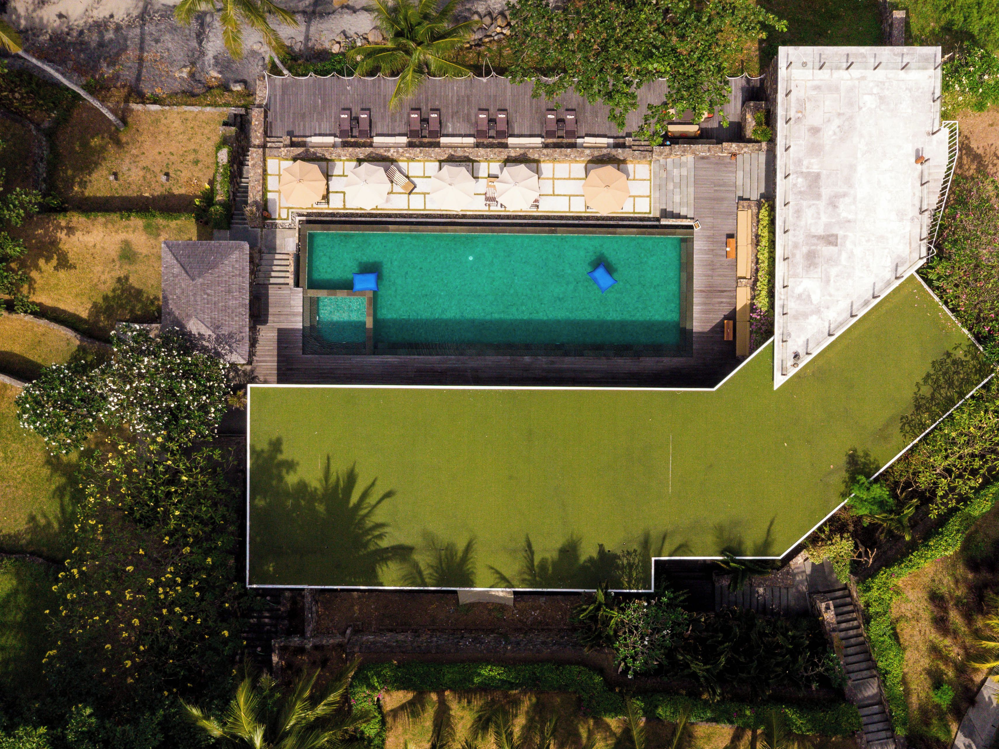 An aerial view of a property with a swimming pool, a covered patio area, and surrounding greenery.