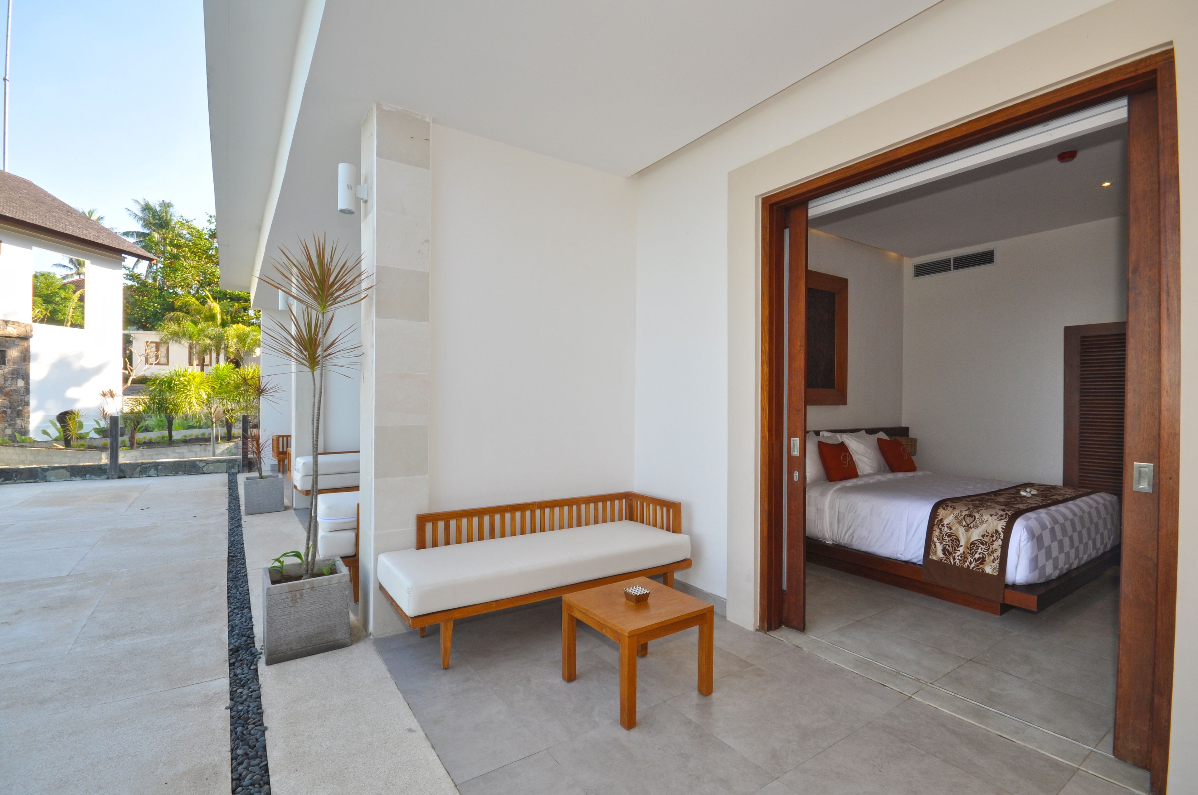 A modern hotel room with a wooden bench, a small table, and a bed with a patterned bedspread.
