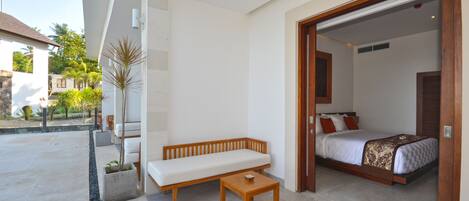 A modern hotel room with a wooden bench, a small table, and a bed with a patterned bedspread.