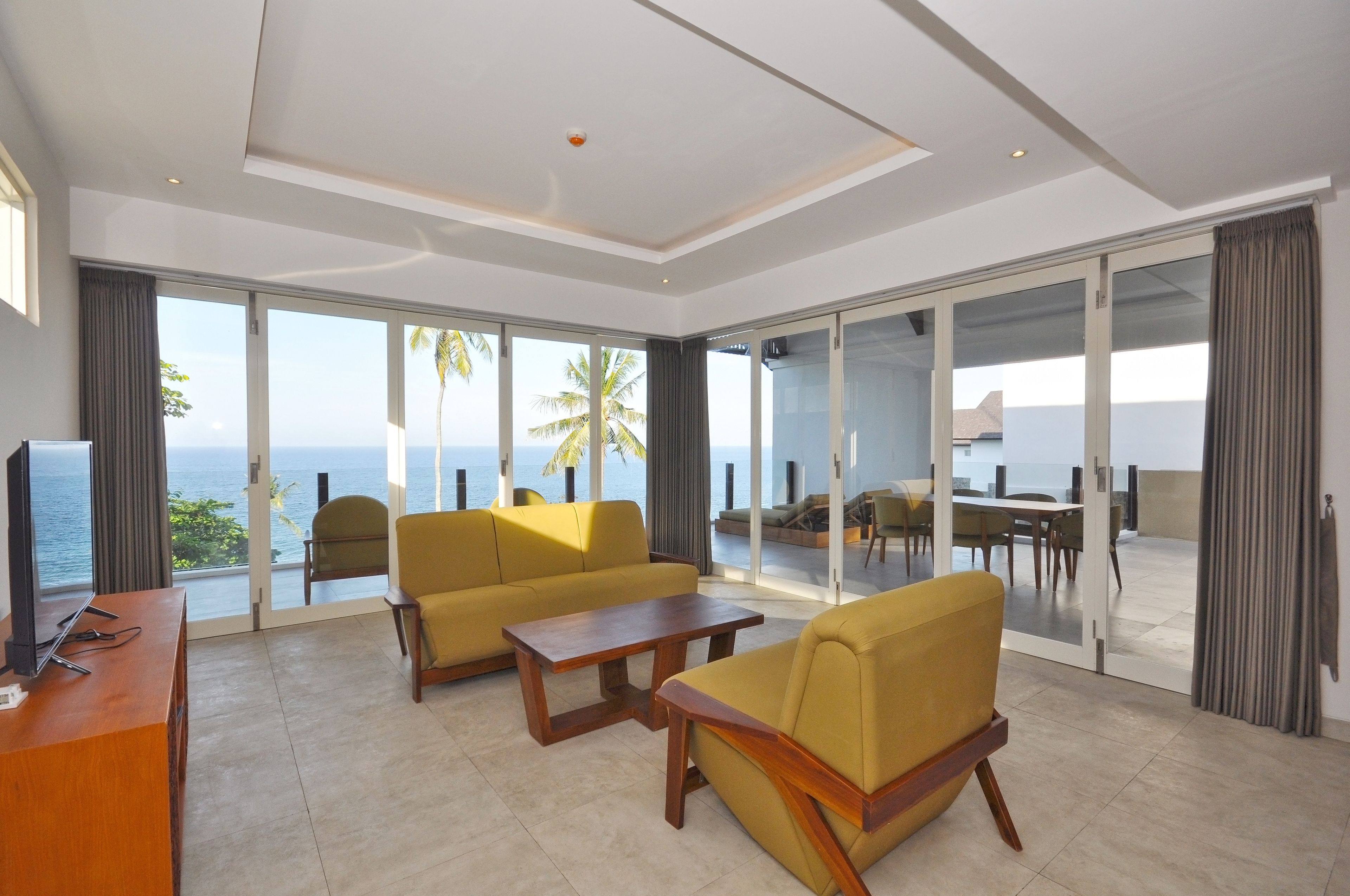 Una sala de estar moderna con ventanas amplias, un sofá, una mesa de centro y un televisor.