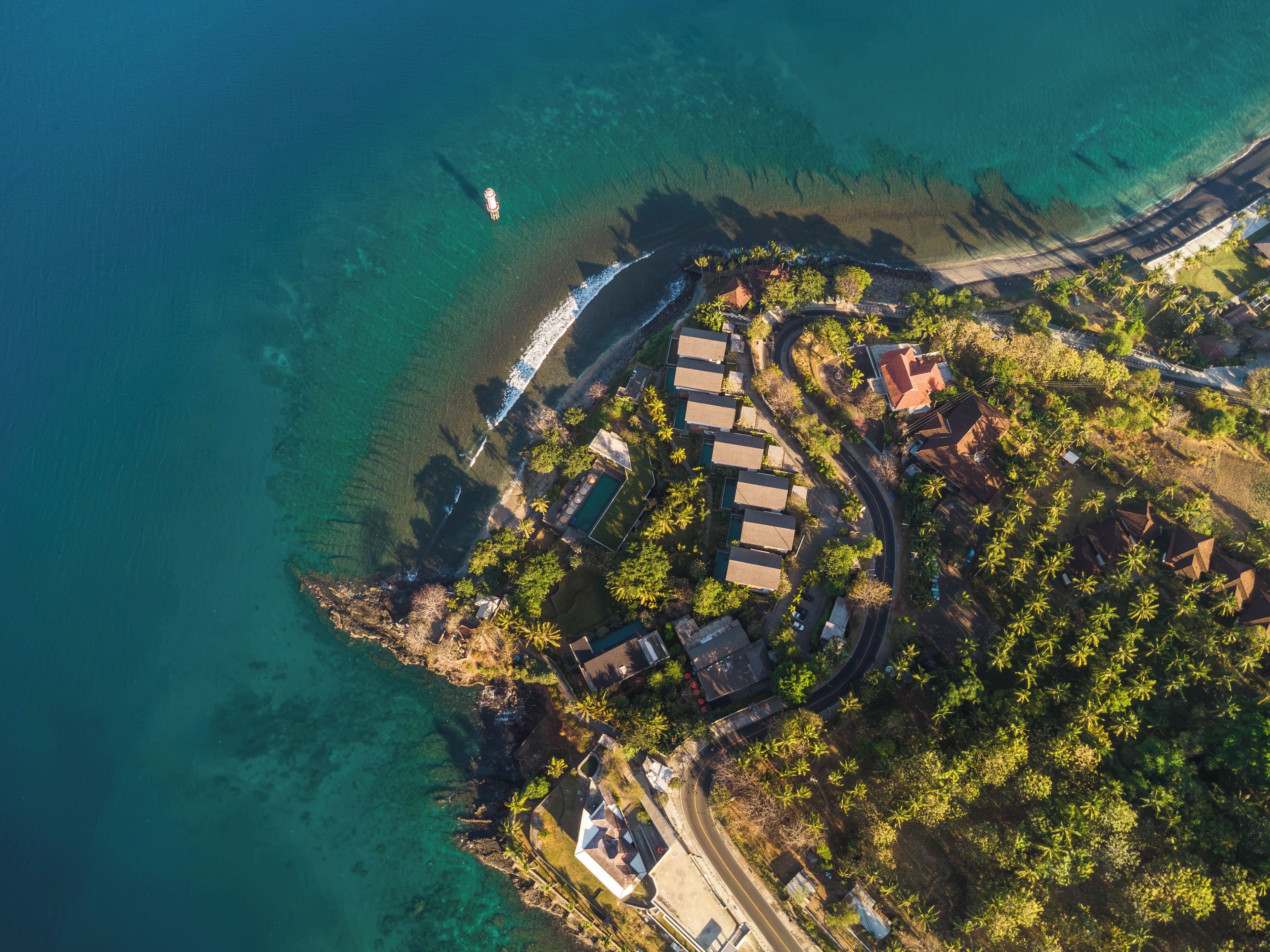 Vista aérea de una propiedad costera con playa despejada, un camino sinuoso y un conjunto de edificios con piscina.