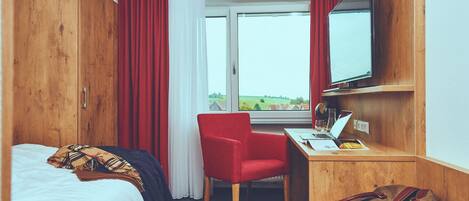 A hotel room with a bed, a desk with a laptop, a chair, and a TV on the wall.