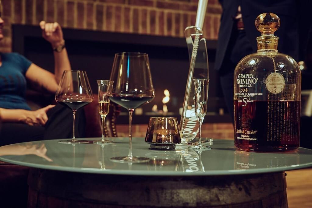 A round table with a bottle of Grappa Nonino Reserva, glasses, and a candle holder.