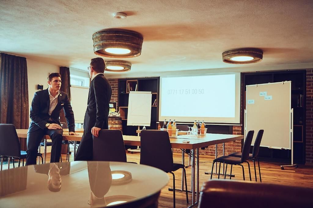 Een vergaderruimte met een grote tafel, stoelen, een whiteboard en een projectiescherm waarop een presentatie wordt getoond.