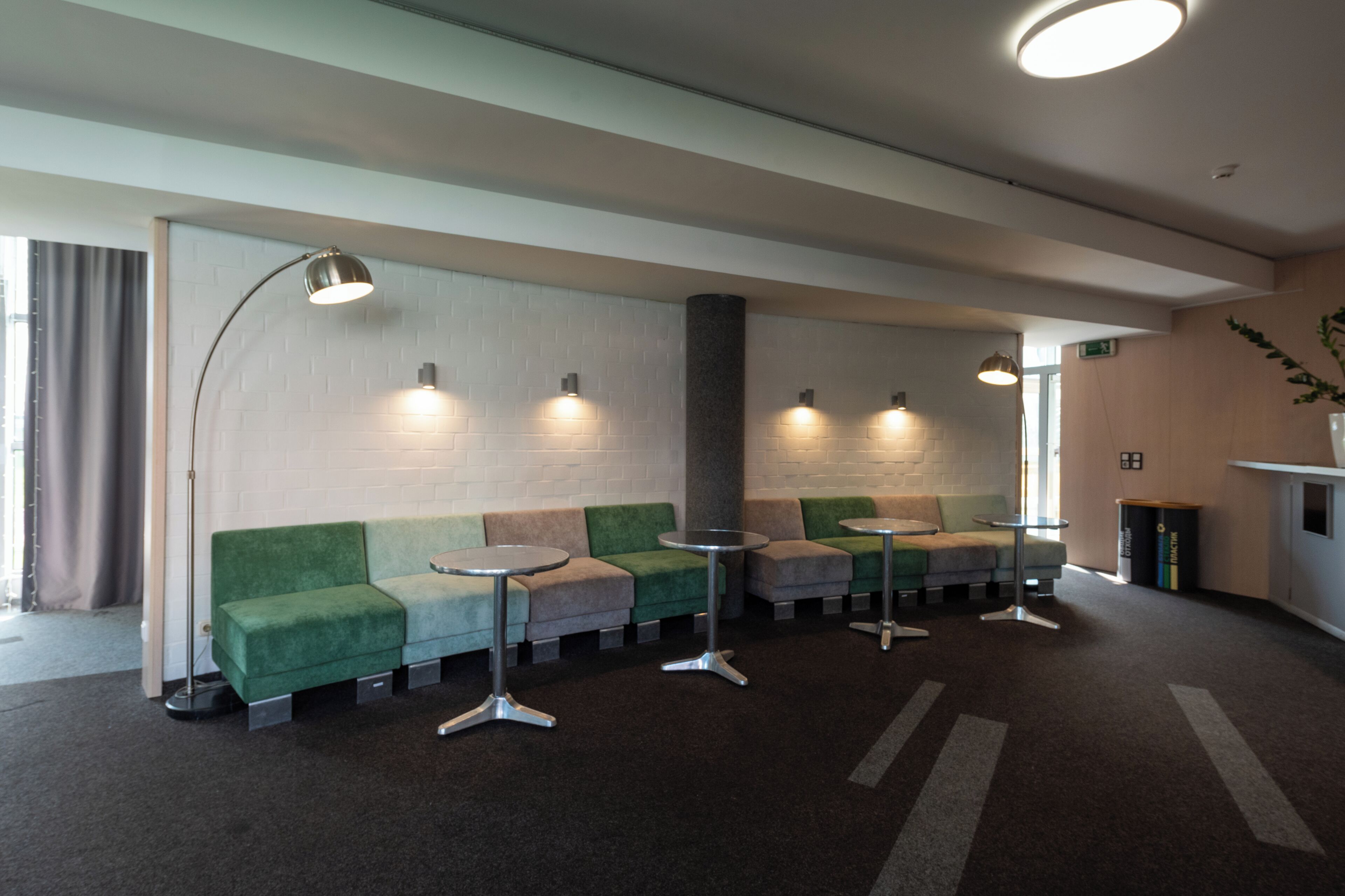 A modern waiting area with green sofas, round tables, and pendant lighting.