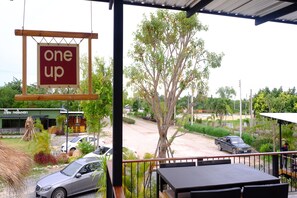 A view from a balcony overlooking a parking area with a 'one up' sign, a building with Thai signage, and a tree.