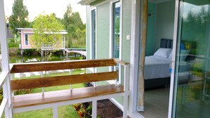 A wooden bench on a porch with a view of a bedroom through a glass door. - Phalagoon Natural Resort @ Rayong (Ban Chang)
