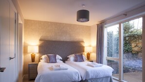 A double room with two beds, bedside tables with lamps, a large window with a view of greenery, and a ceiling light fixture. - Beech House (Bristol)
