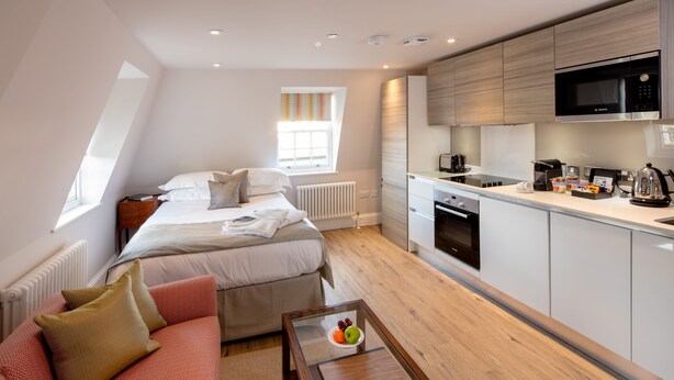 A modern bedroom with a large bed, a sofa, and a breakfast bar with kitchen appliances. - Beech House (Bristol)