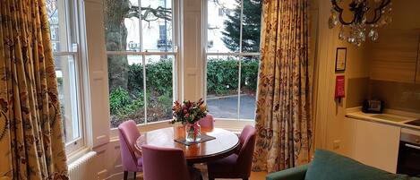 A room with a dining table and chairs, a sofa, a chandelier, and large windows with curtains.