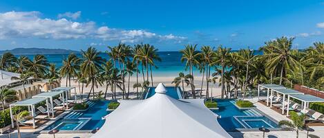 A resort with a central swimming pool, palm trees, and a beach view.