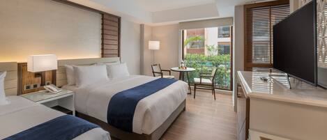 A hotel room with two beds, a desk with a lamp, a TV, and a balcony with a table and chairs.