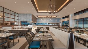 A modern restaurant with high ceilings, pendant lighting, and a mix of seating options including booths and tables.