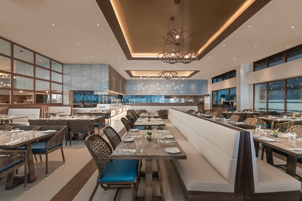 A modern restaurant with high ceilings, pendant lighting, and a mix of seating options including booths and tables.