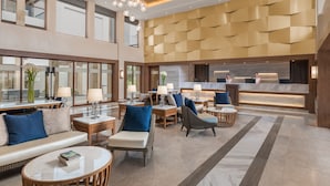 A spacious lobby with a modern design, featuring a reception desk, seating areas, and large windows.