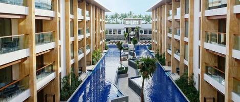 A modern hotel with a central swimming pool, multiple floors, and a tropical garden setting.