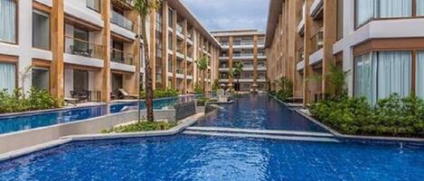 A swimming pool with a tiled floor, surrounded by multi-story buildings with balconies and windows.