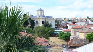 A view of a town with a prominent church featuring a dome and bell tower, surrounded by residential buildings with red-tiled roofs. - Mercanay Butik Otel (Ayvalik)