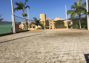 A sandy sports court with a goalpost, surrounded by a fence and palm trees, with a building in the background. - Hotel Morro do Sol (Porto Belo)