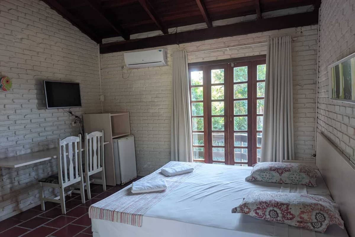Une chambre à coucher comprenant un lit, une télévision, un bureau et une fenêtre donnant sur un paysage verdoyant.