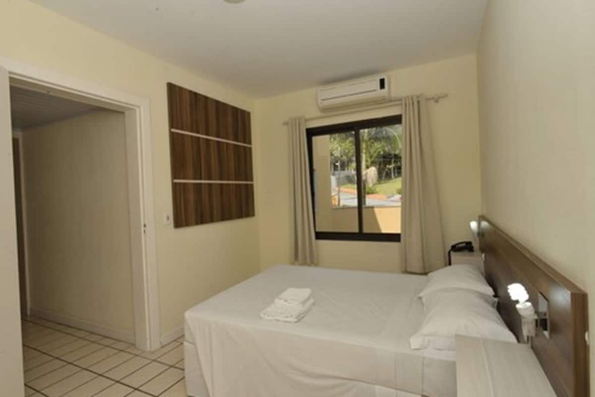 Une chambre d’hôtel avec un lit, une fenêtre avec des rideaux, un appareil de climatisation et un panneau en bois sur le mur.