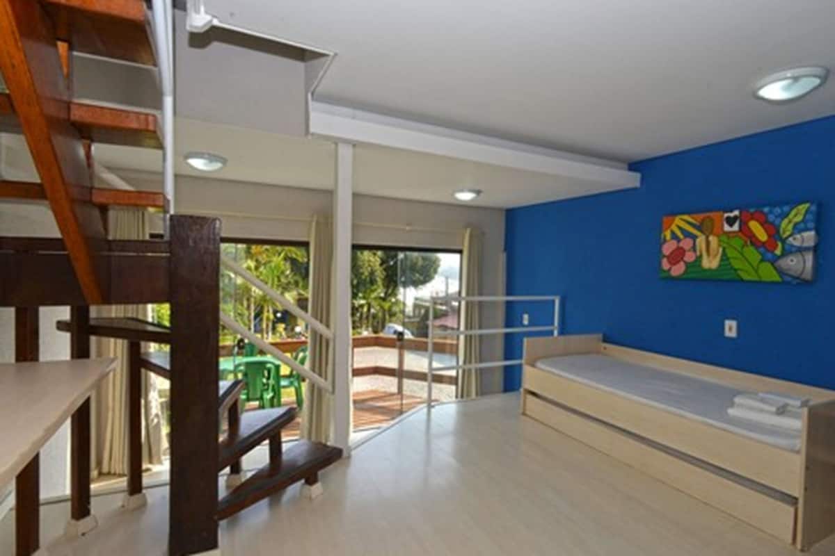 Une chambre avec un lit superposé, un escalier et une vue sur un espace extérieur verdoyant.